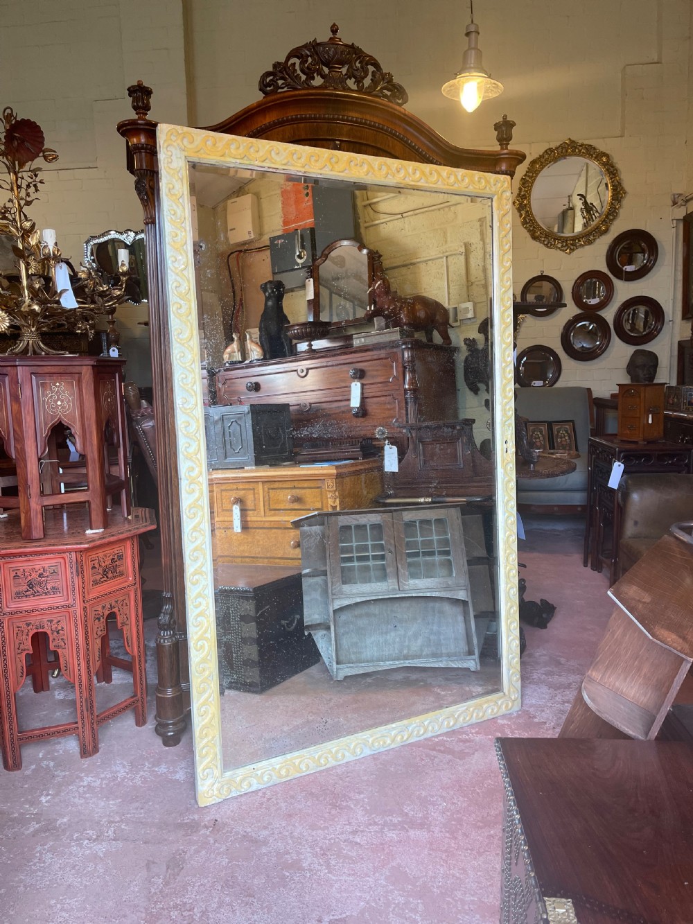 A large rectangular wall mirror featuring a cream-painted wooden frame decorated with a continuous carved Vitruvian scroll wave motif along all four sides.