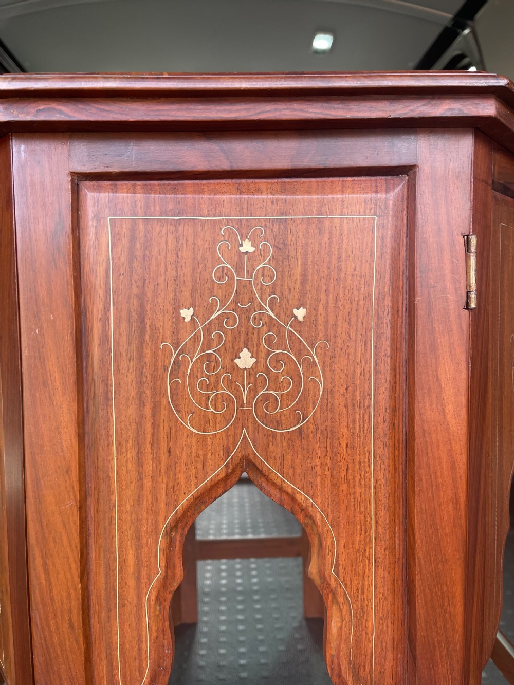 An octagonal warm brown wooden side table with delicate brass wire inlays and pointed arch cut-outs around the base. View V