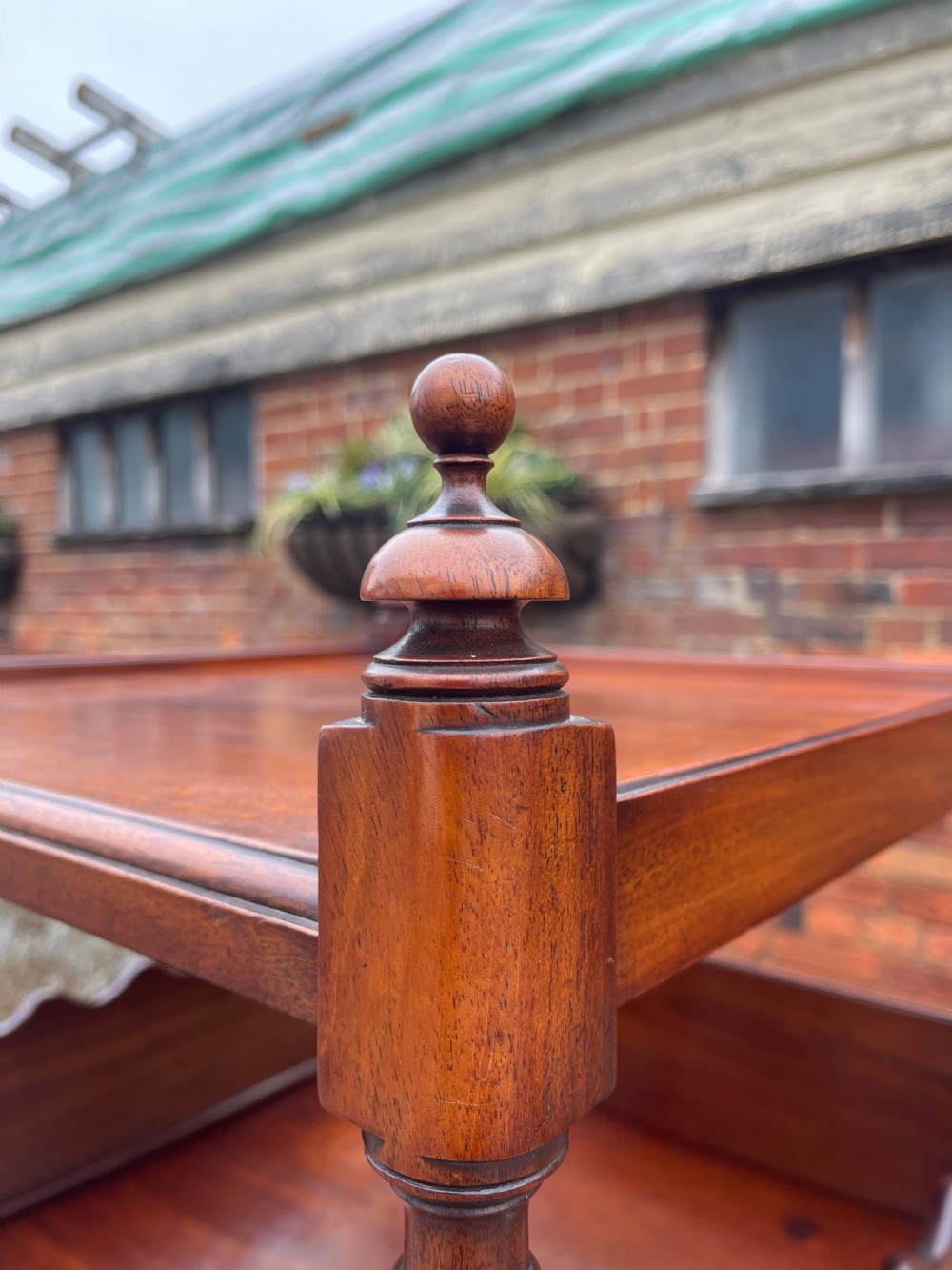 A nineteenth-century mahogany cupboard base whatnot featuring open shelves supported by turned posts, a single drawer, and a lower cabinet with an arched flame mahogany panel on brass castors. View II