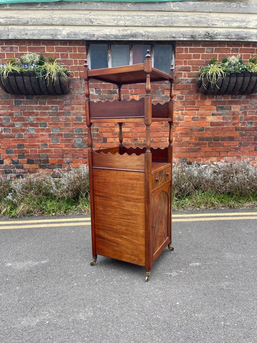 A nineteenth-century mahogany cupboard base whatnot featuring open shelves supported by turned posts, a single drawer, and a lower cabinet with an arched flame mahogany panel on brass castors. View III
