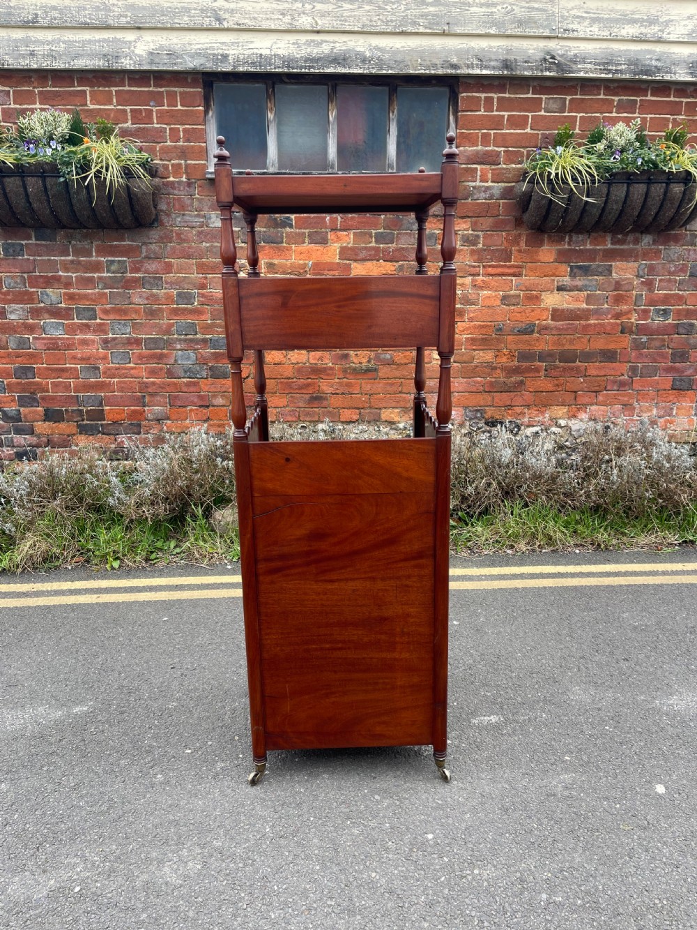 A nineteenth-century mahogany cupboard base whatnot featuring open shelves supported by turned posts, a single drawer, and a lower cabinet with an arched flame mahogany panel on brass castors. View VI