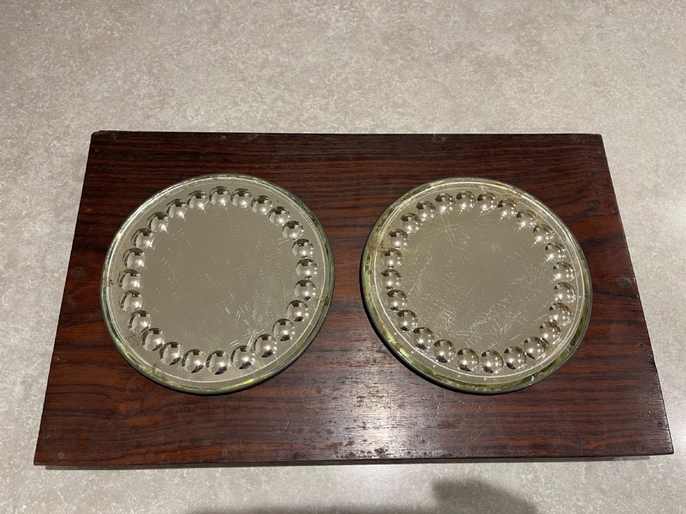 A pair of circular sorcerer-style glass plateau mirrors featuring raised cabochon borders resting on a dark wood panel.