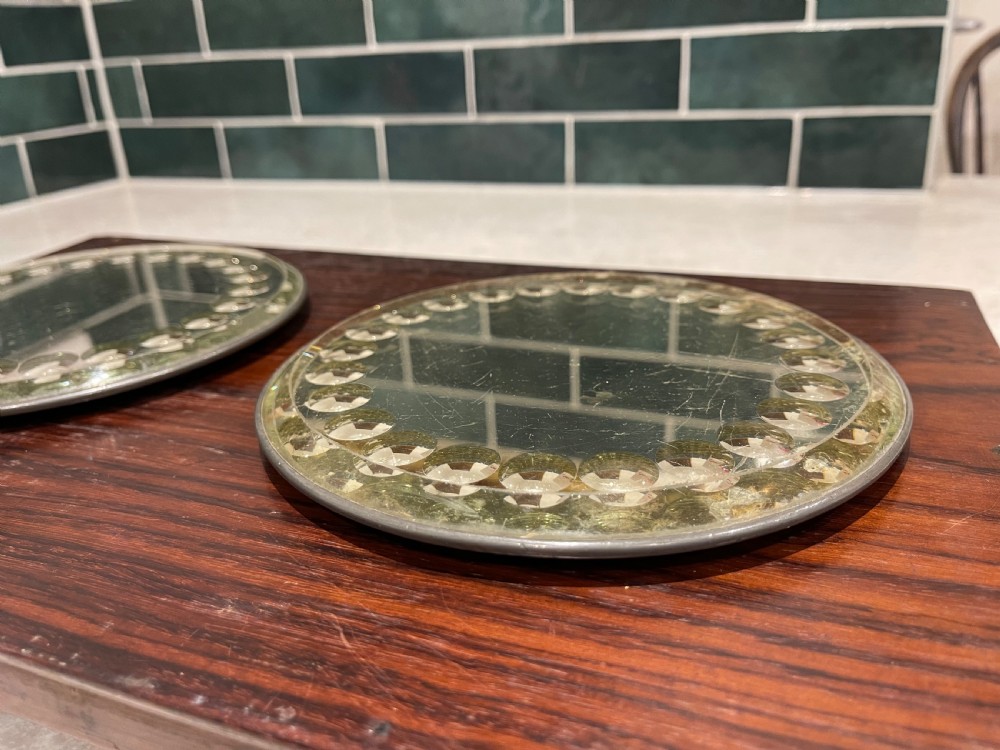 A pair of circular sorcerer-style glass plateau mirrors featuring raised cabochon borders resting on a dark wood panel. View III
