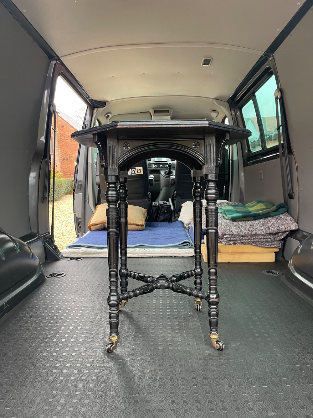 An Aesthetic Movement ebonised wooden side table featuring turned legs, cross stretchers, an arched apron with rosettes, and brass castors.