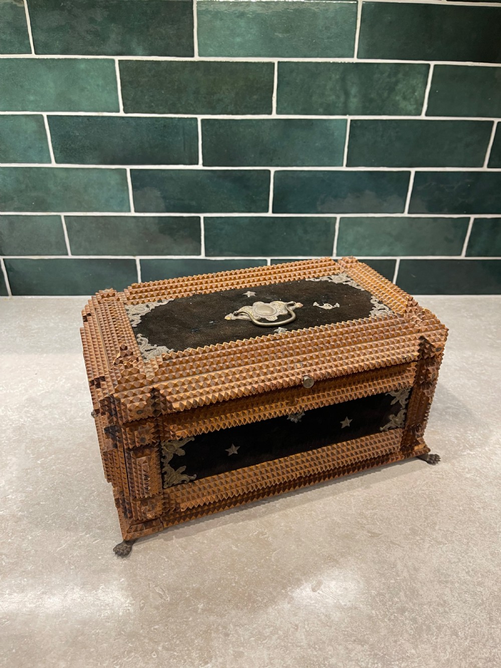 An antique tramp art box featuring layered notch-carved brown wood, dark velvet panels, metal corner mounts, and claw feet.