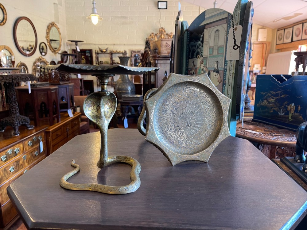 A pair of engraved brass trays, each supported by a detailed coiled cobra pedestal stem.