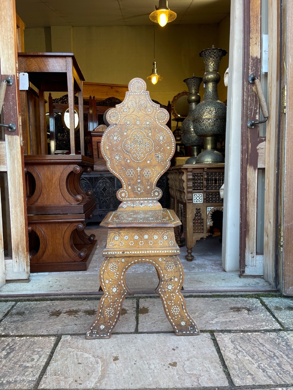 A dark timber hall chair featuring intricate white bone inlay in geometric and floral patterns along the contoured backrest, seat, and trestle legs.