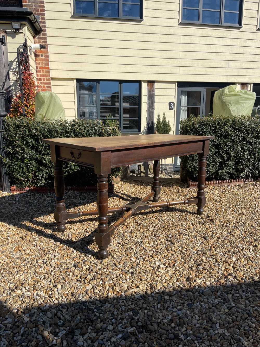 A nineteenth-century rectangular dark oak table featuring turned legs, a turned X-frame stretcher base, and a side drawer.