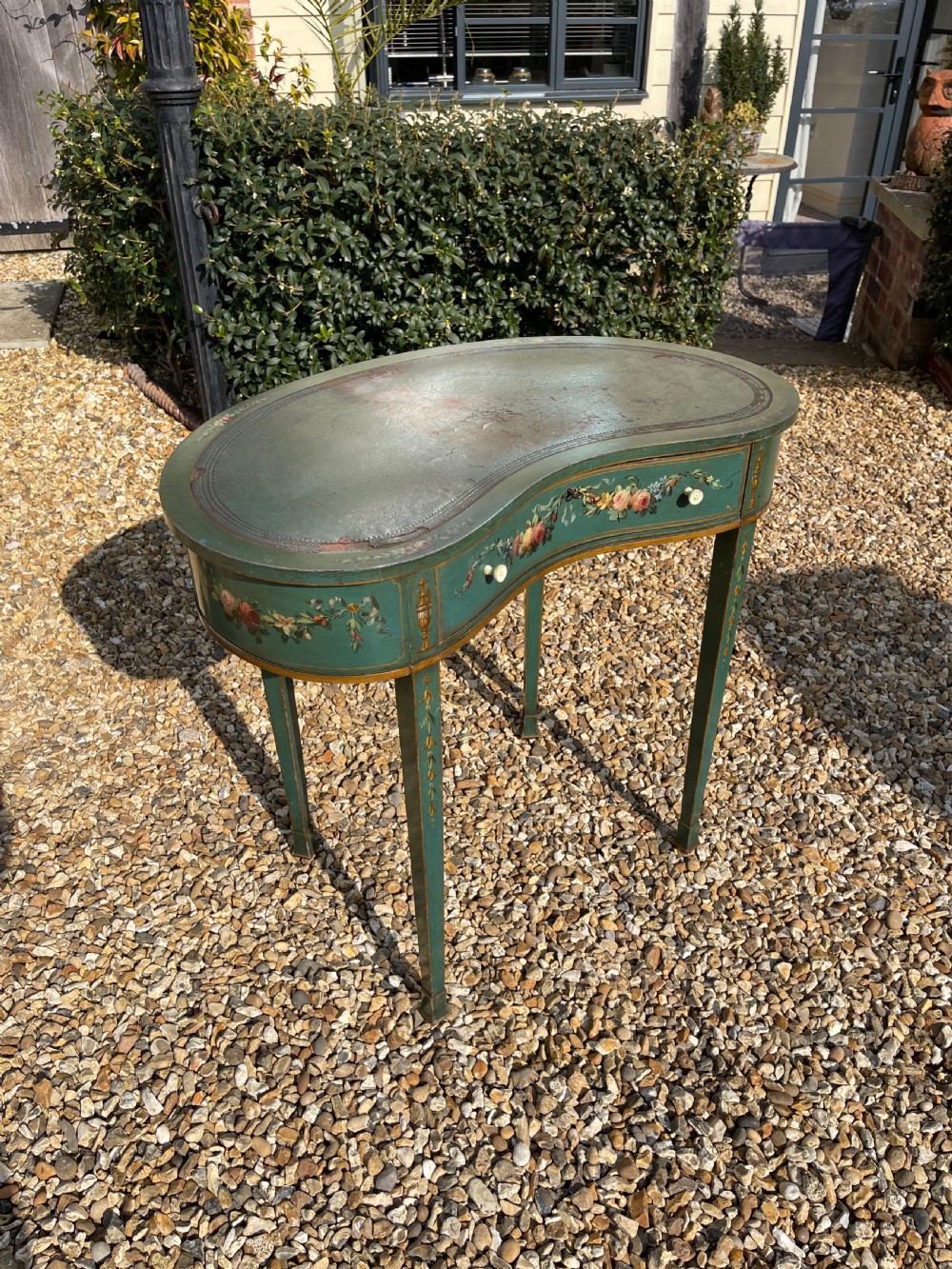 A late Victorian kidney-shaped writing desk finished in green paint with hand-painted floral swags and an inset leather top.
