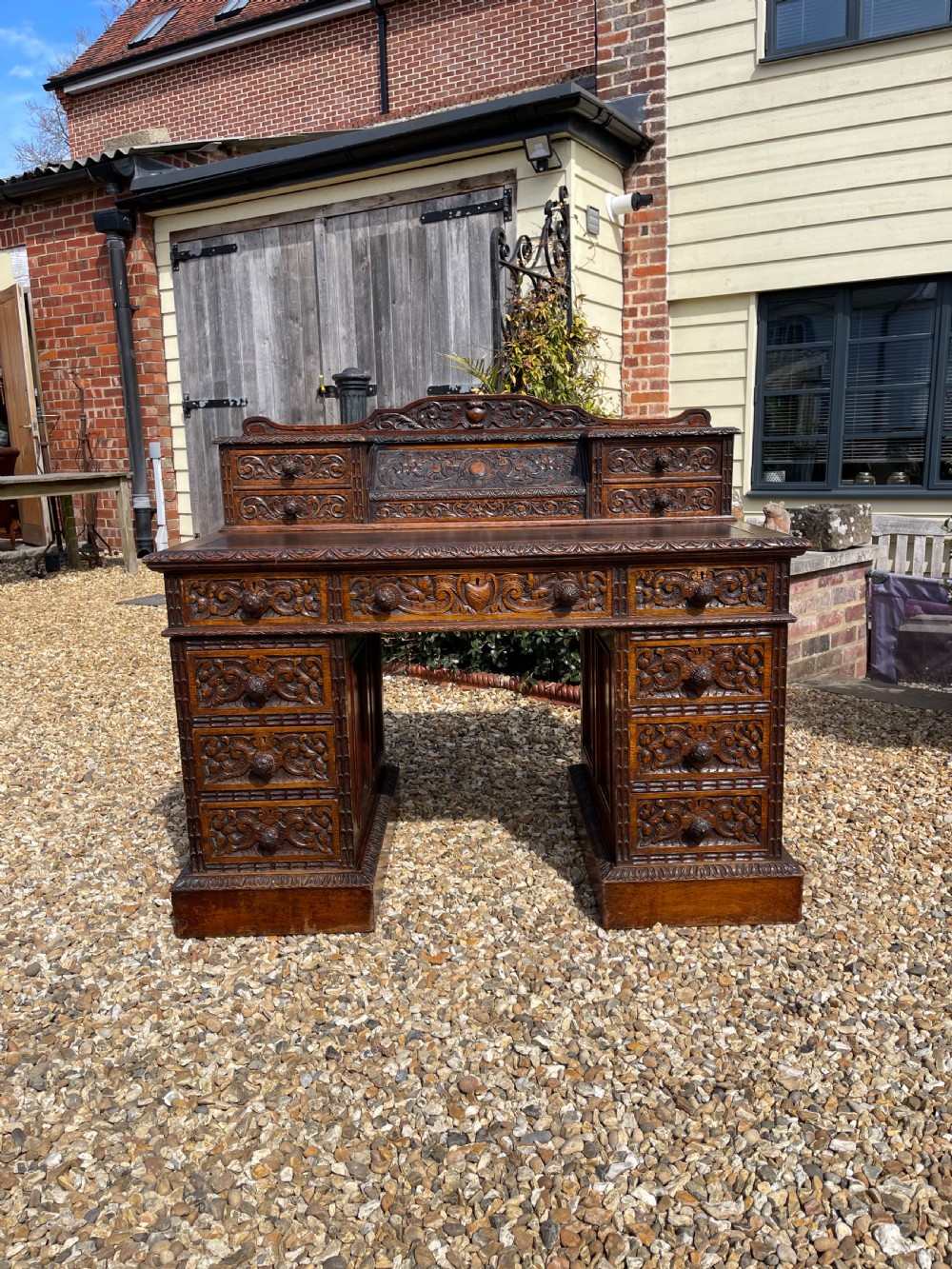 A late Victorian dark oak pedestal desk featuring intricate relief carving across all drawer fronts and a detailed raised superstructure.