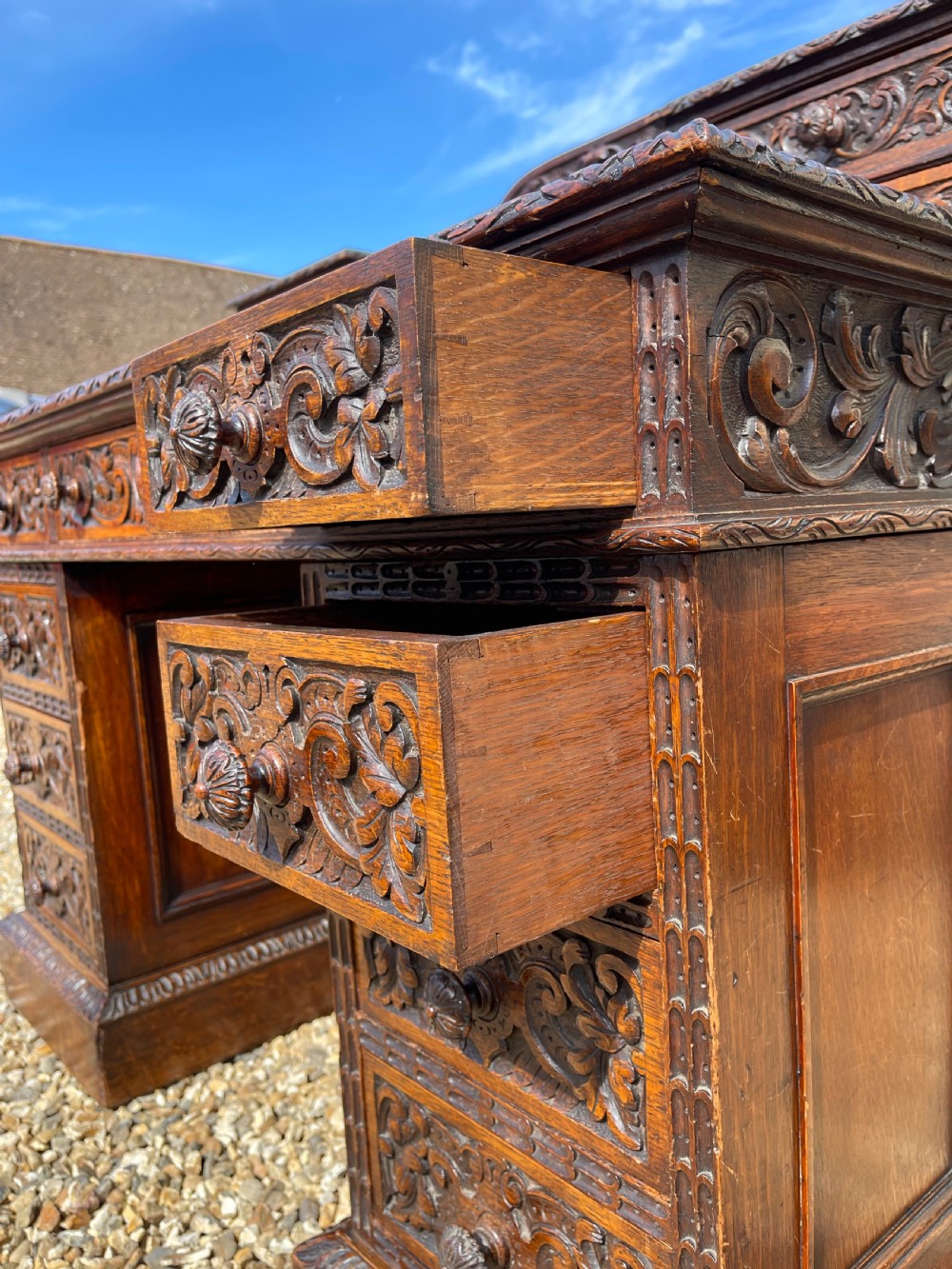 A late Victorian dark oak pedestal desk featuring intricate relief carving across all drawer fronts and a detailed raised superstructure. View X