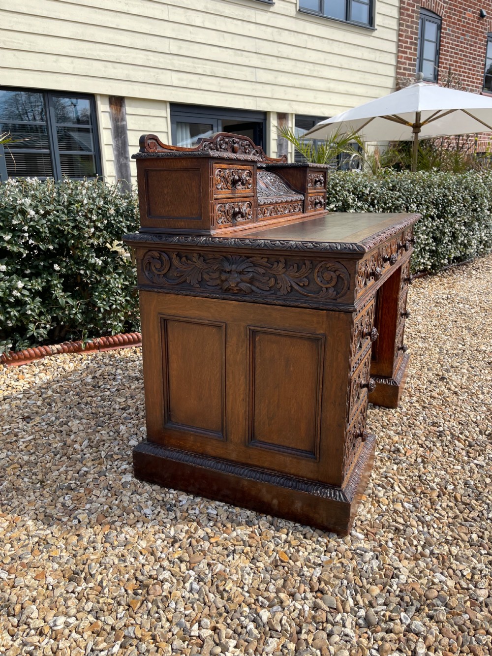 A late Victorian dark oak pedestal desk featuring intricate relief carving across all drawer fronts and a detailed raised superstructure. View XI