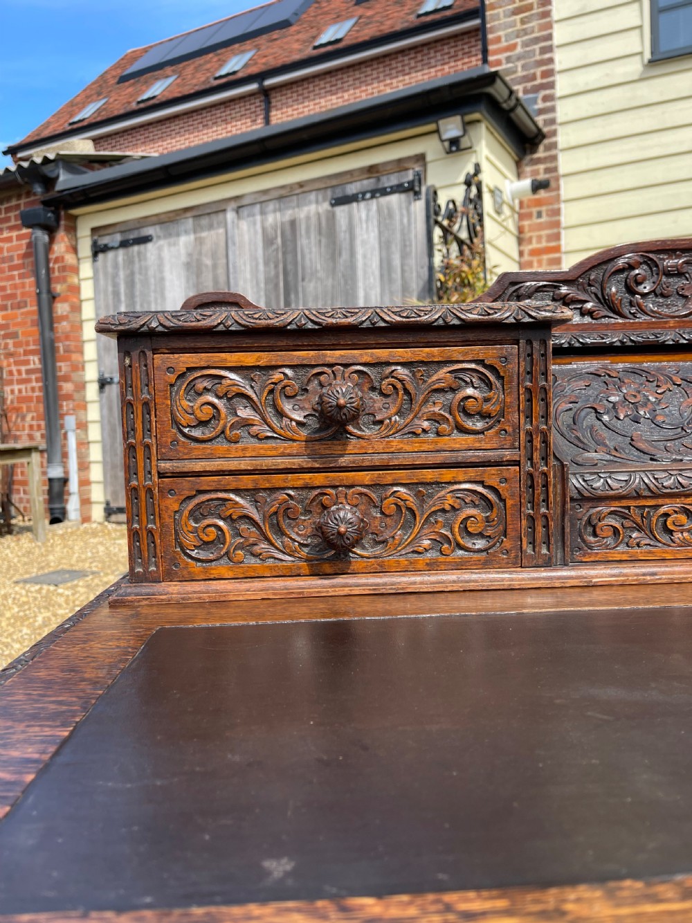 A late Victorian dark oak pedestal desk featuring intricate relief carving across all drawer fronts and a detailed raised superstructure. View XV