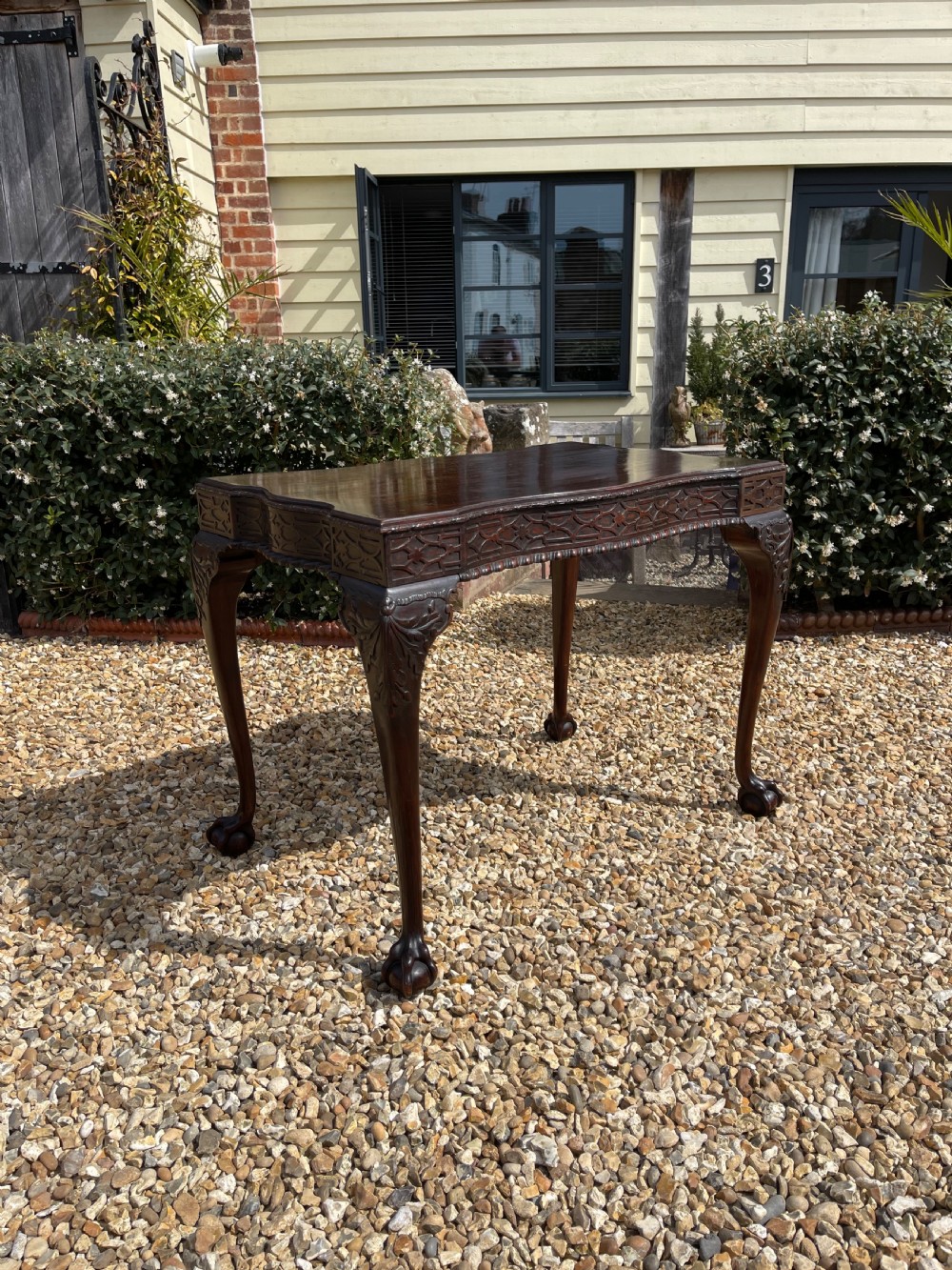 A dark mahogany Chippendale style side table featuring carved ball-and-claw feet, carved knees, and a blind fretwork apron.