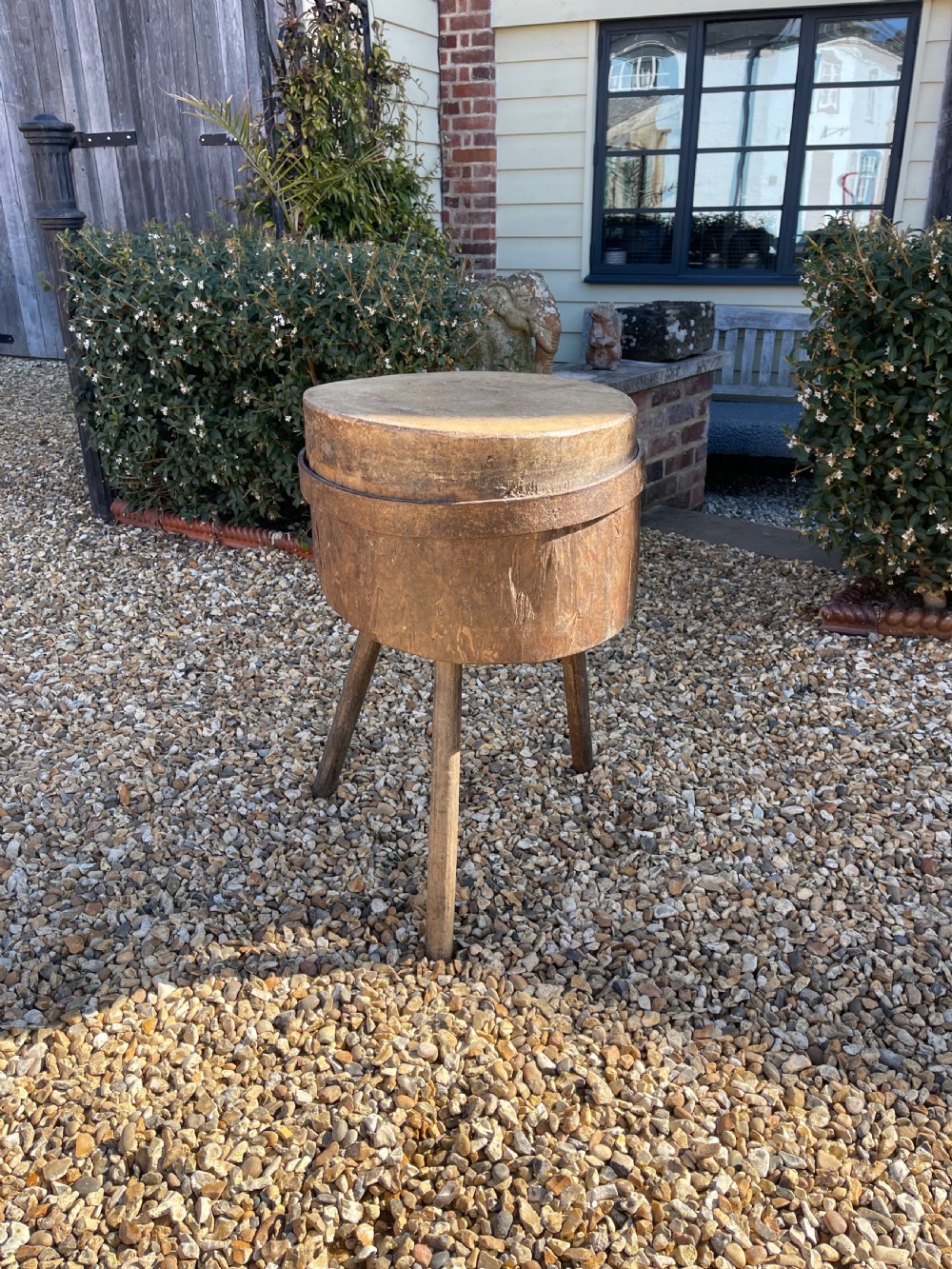 A circular antique wooden butcher block featuring a thick end-grain top set upon three splayed wooden legs.