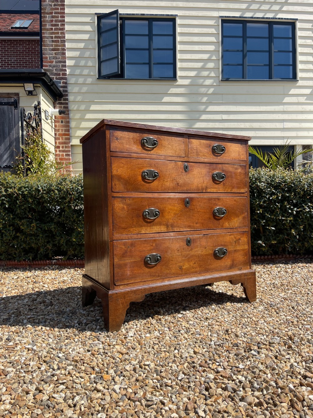 A George III wooden chest of drawers featuring two short drawers over three long graduated drawers, fitted with brass handles and supported on bracket feet.