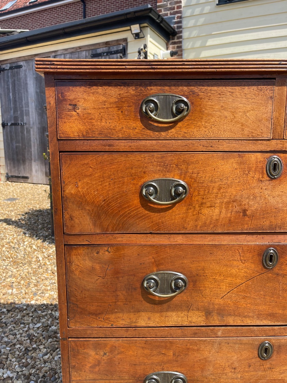 A George III wooden chest of drawers featuring two short drawers over three long graduated drawers, fitted with brass handles and supported on bracket feet. View II