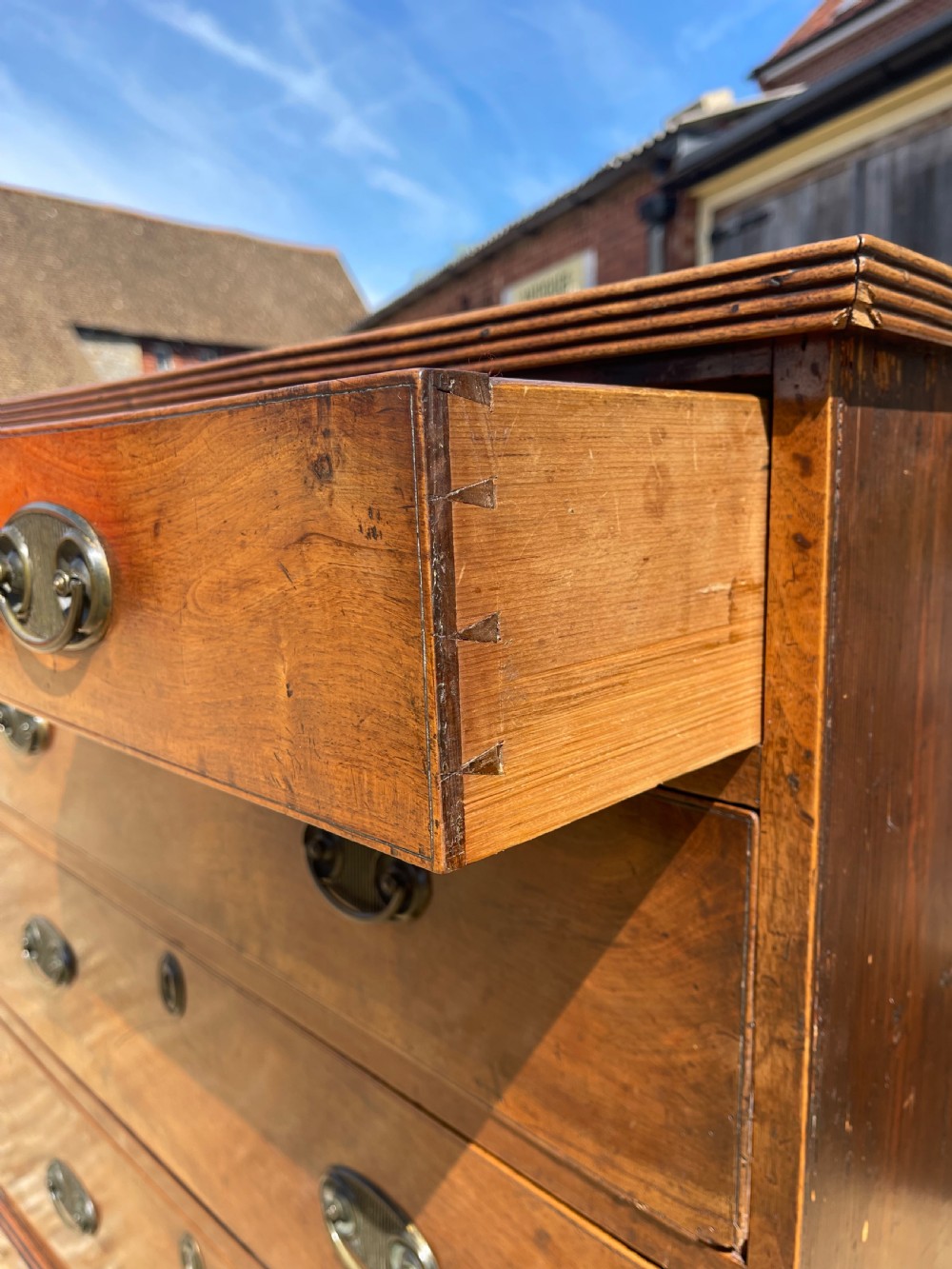 A George III wooden chest of drawers featuring two short drawers over three long graduated drawers, fitted with brass handles and supported on bracket feet. View III