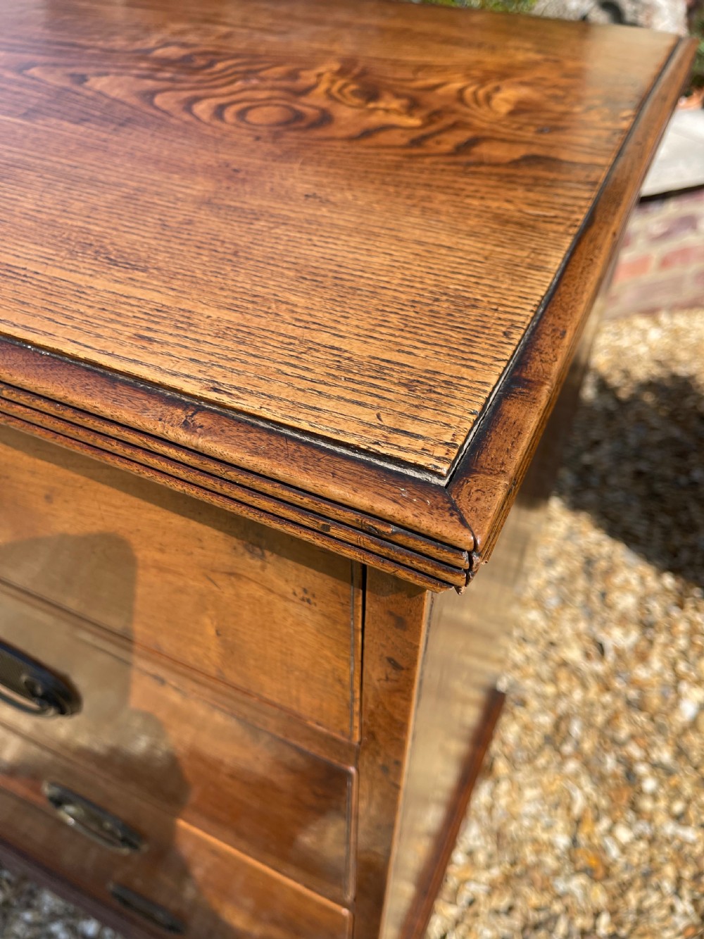 A George III wooden chest of drawers featuring two short drawers over three long graduated drawers, fitted with brass handles and supported on bracket feet. View V