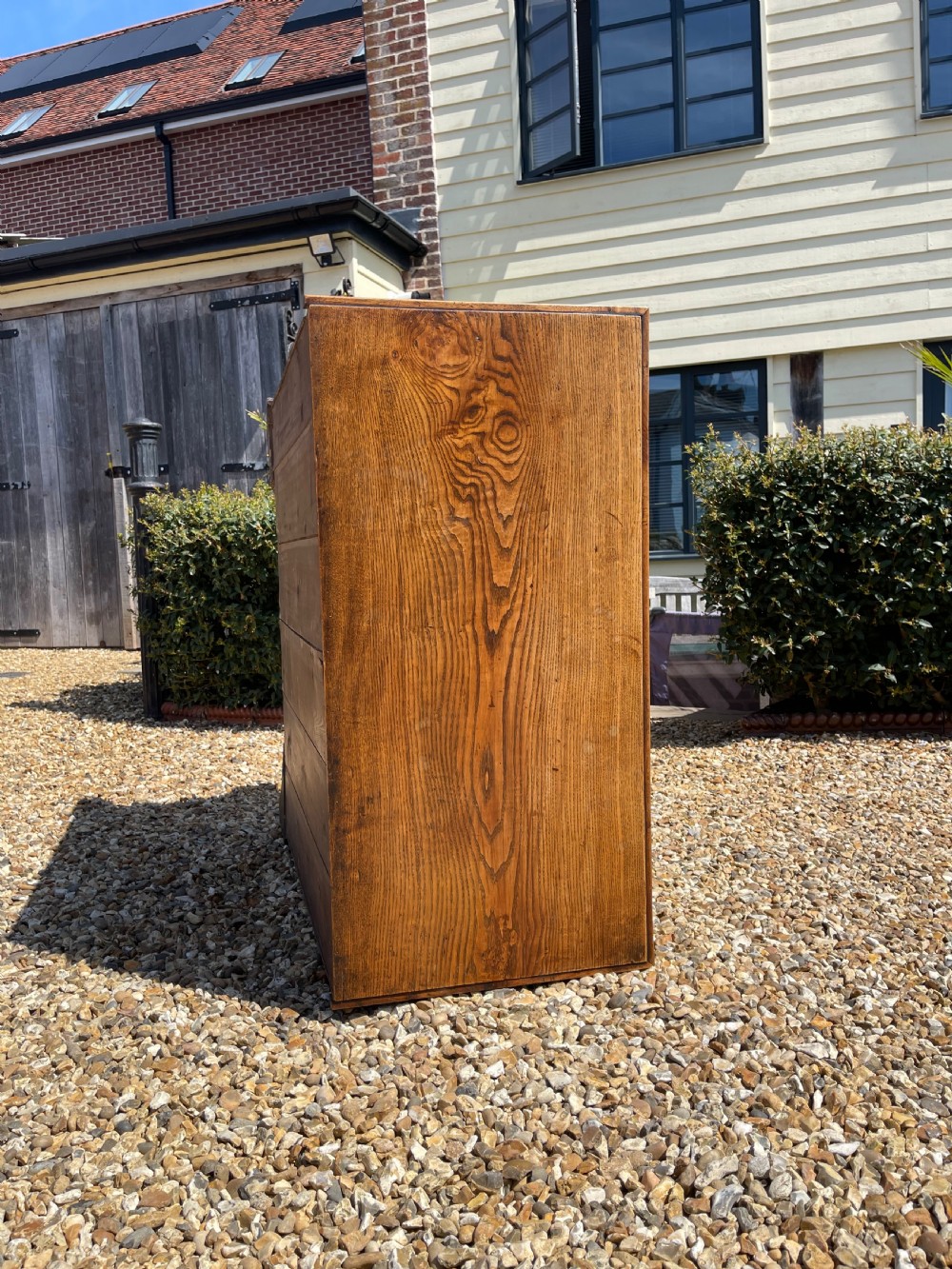 A George III wooden chest of drawers featuring two short drawers over three long graduated drawers, fitted with brass handles and supported on bracket feet. View X