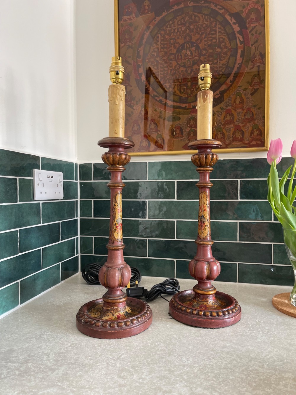 A pair of tall Italian carved wooden candlestick table lamps decorated with terracotta red paint, gold leaf accents, and faux candle sleeves.