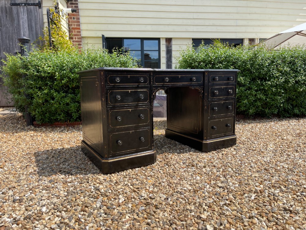 A nineteenth-century ebonised pedestal desk featuring fine gilt line decoration, turned drawer handles, and twin pedestals flanking a central kneehole.