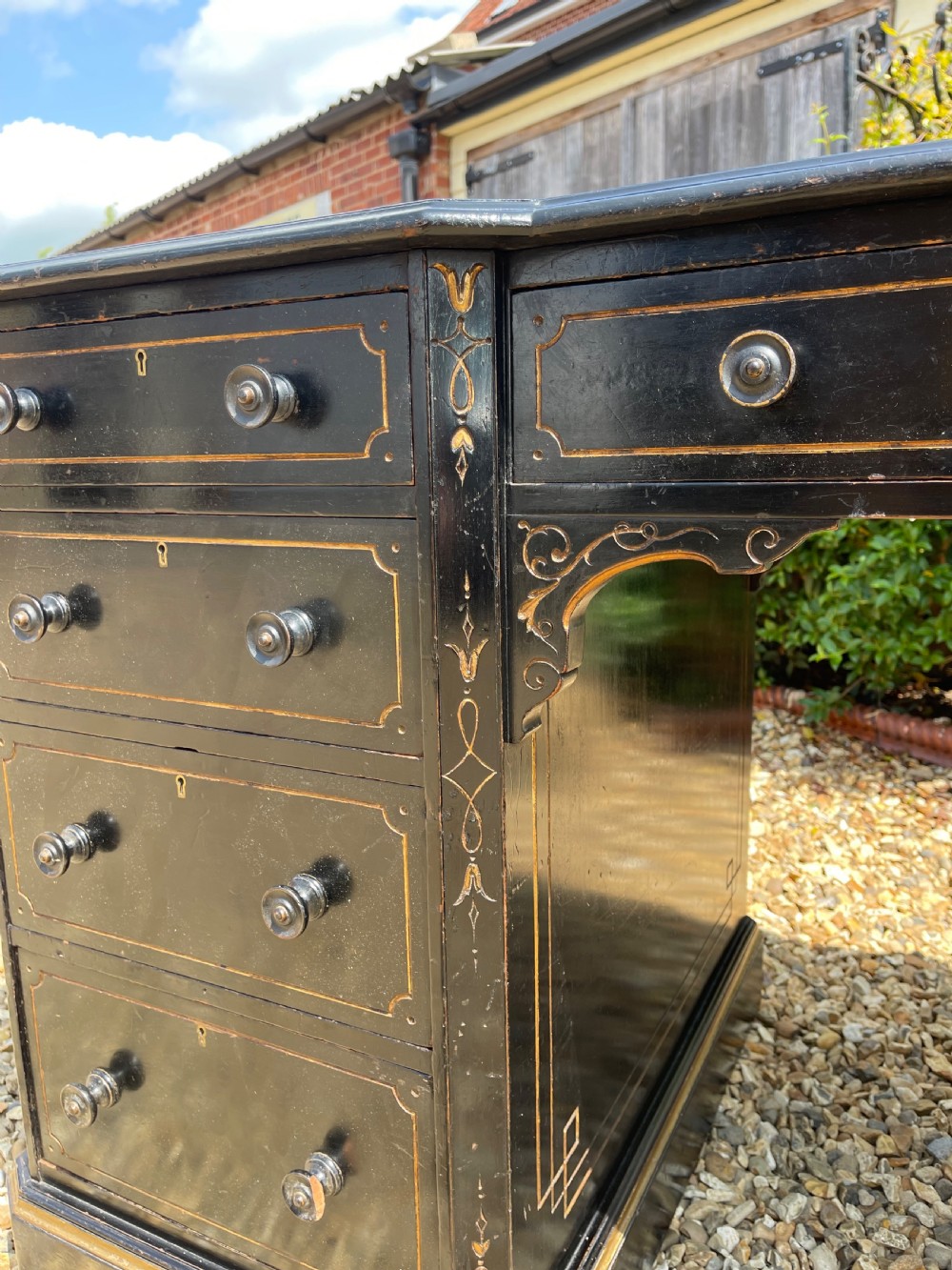 A nineteenth-century ebonised pedestal desk featuring fine gilt line decoration, turned drawer handles, and twin pedestals flanking a central kneehole. View X