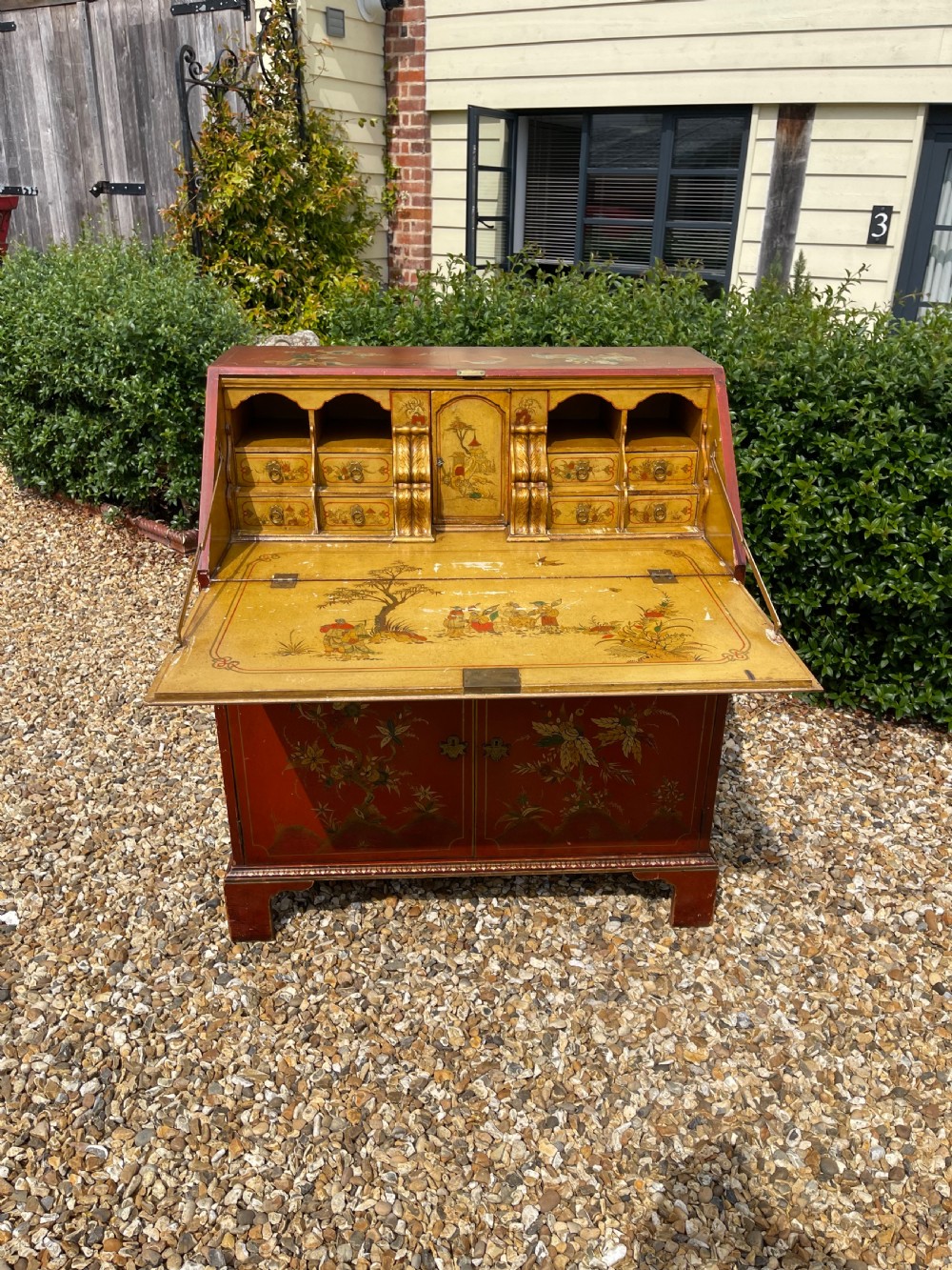 An antique red lacquered fall-front bureau with hand-painted Chinoiserie scenes and a yellow fitted interior featuring cubbies and small drawers. View II