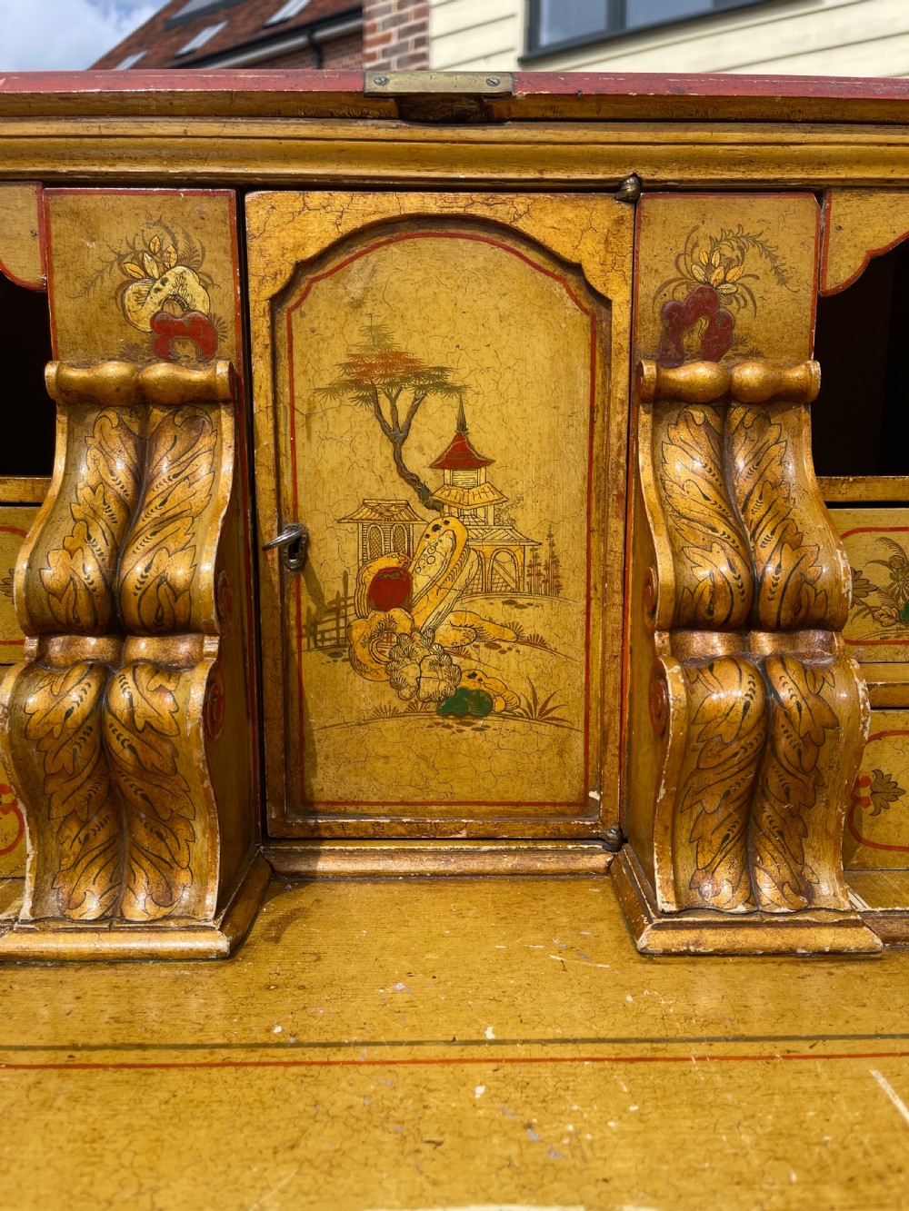 An antique red lacquered fall-front bureau with hand-painted Chinoiserie scenes and a yellow fitted interior featuring cubbies and small drawers. View X