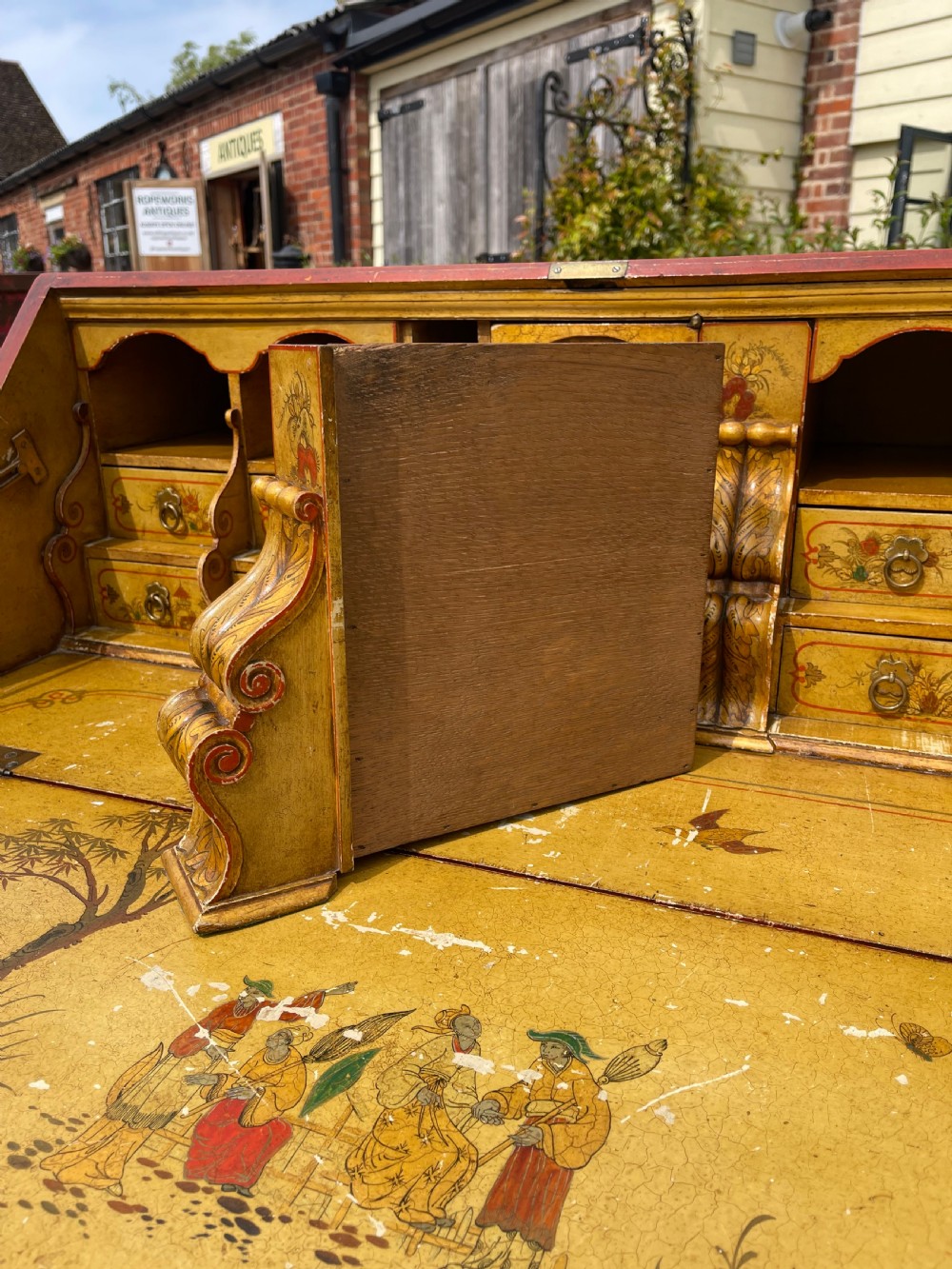An antique red lacquered fall-front bureau with hand-painted Chinoiserie scenes and a yellow fitted interior featuring cubbies and small drawers. View XI
