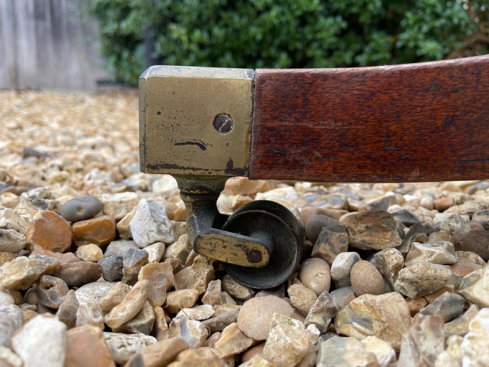 An oval George III mahogany breakfast table with crossbanded satinwood border on a central pedestal base with four splayed legs terminating in brass castors. View II