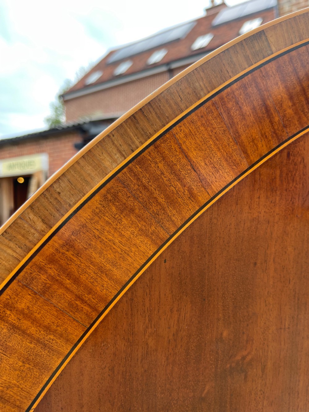 An oval George III mahogany breakfast table with crossbanded satinwood border on a central pedestal base with four splayed legs terminating in brass castors. View IV