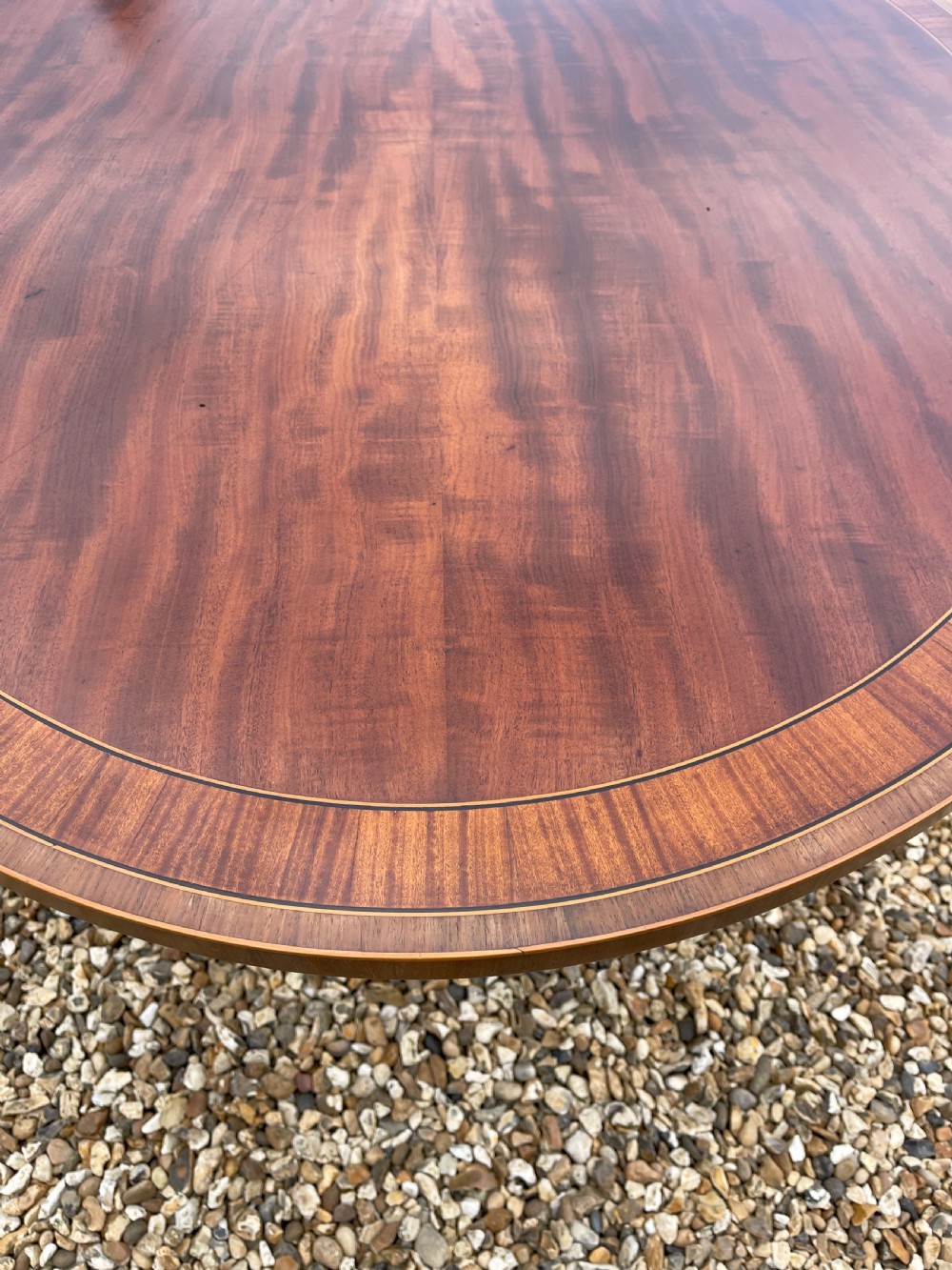 An oval George III mahogany breakfast table with crossbanded satinwood border on a central pedestal base with four splayed legs terminating in brass castors. View VII