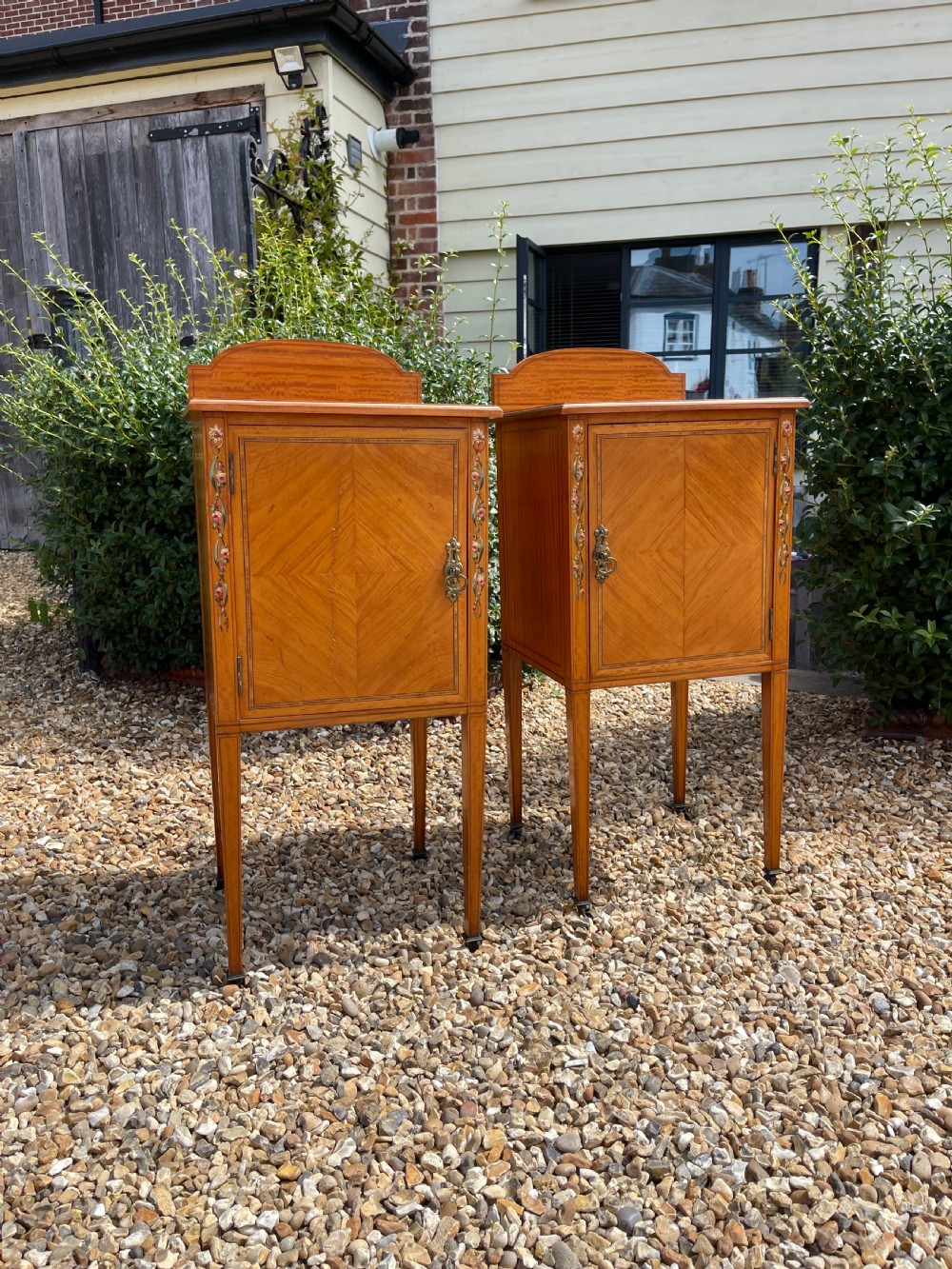 A pair of Edwardian satinwood bedside cupboards featuring diamond marquetry door panels, hand-painted floral stiles, and square tapered legs.