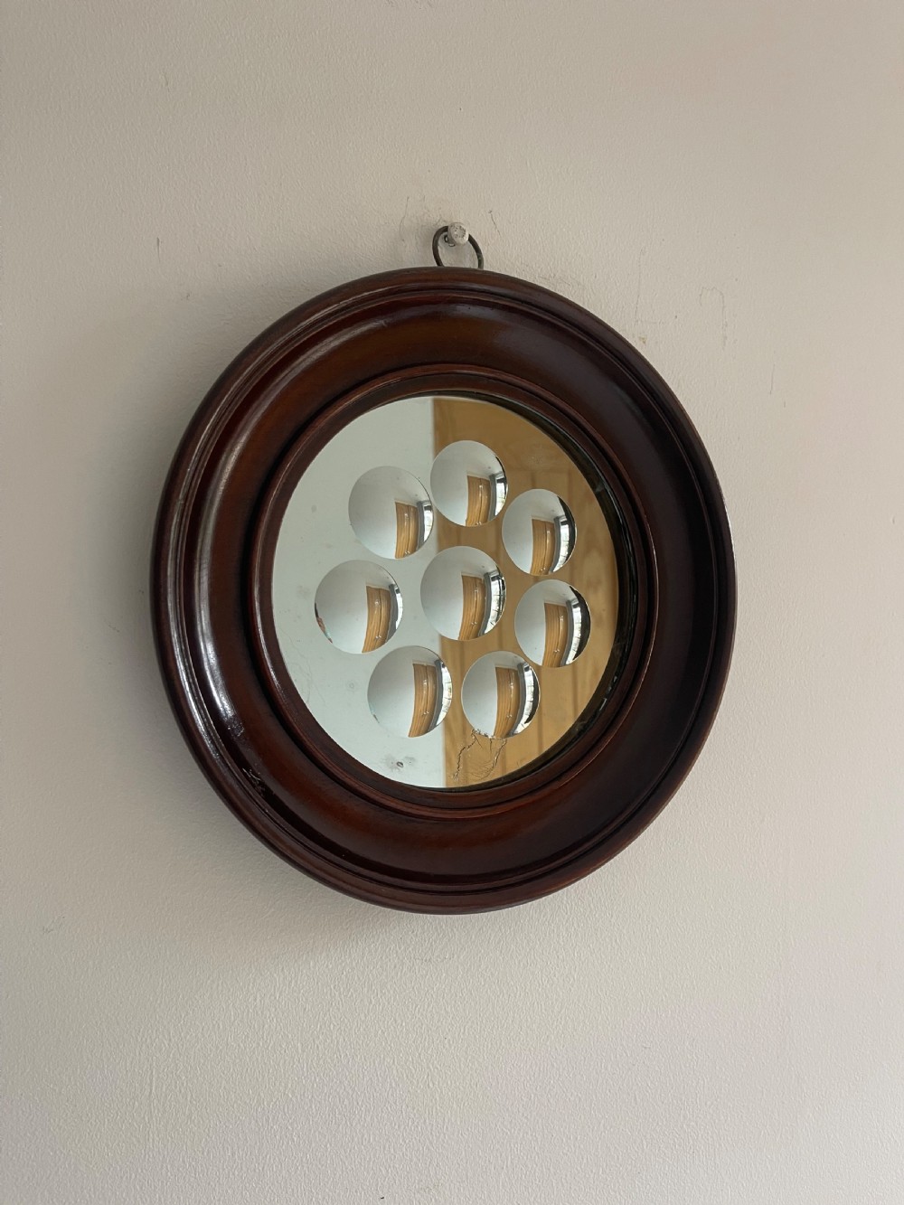 A circular dark mahogany framed wall mirror featuring a central reflective pane set with eight ground circular convex lenses.