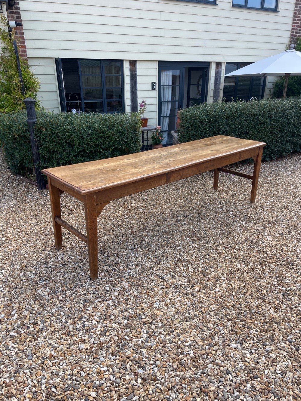 A long antique elm refectory table featuring a natural wood grain finish, straight legs, and end stretchers.