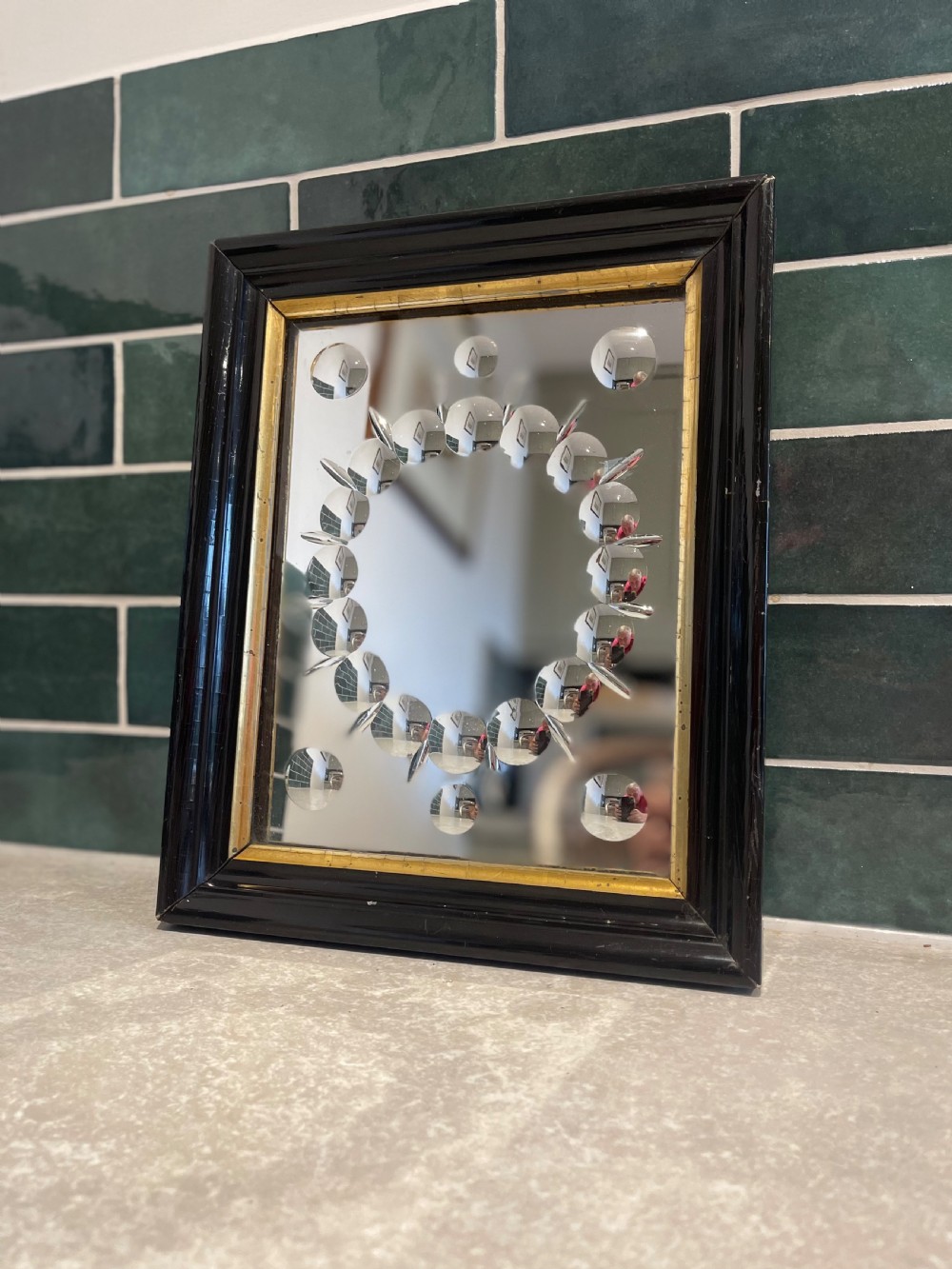 A rectangular black ebonised wall mirror featuring a gold gilt inner moulding and a central ring of circular convex glass cabochons.