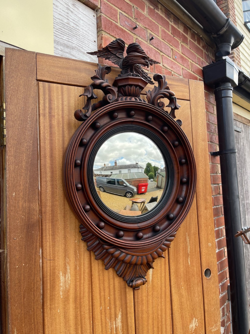 A carved dark timber convex wall mirror featuring a crested eagle surmount, spherical frame embellishments, and a circular convex glass plate.