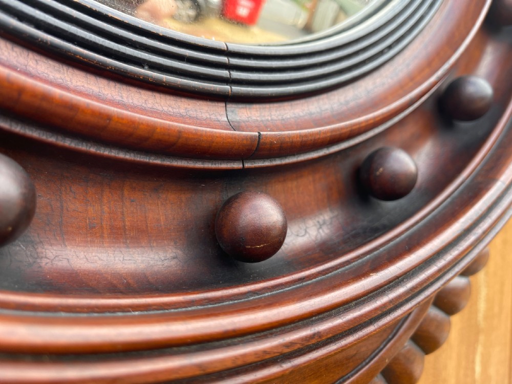 A carved dark timber convex wall mirror featuring a crested eagle surmount, spherical frame embellishments, and a circular convex glass plate. View II