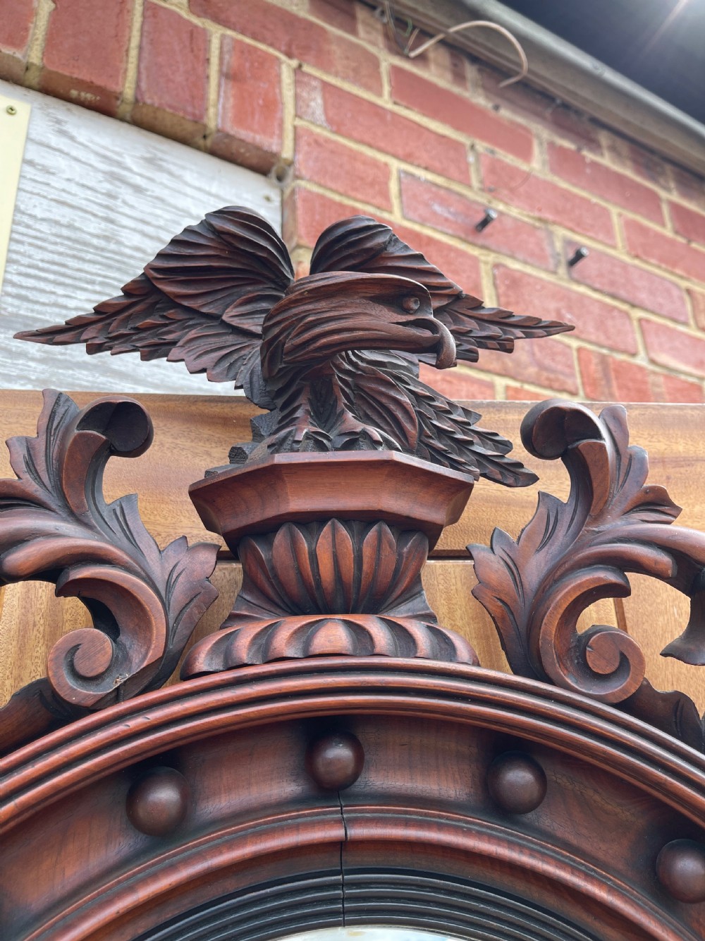 A carved dark timber convex wall mirror featuring a crested eagle surmount, spherical frame embellishments, and a circular convex glass plate. View III