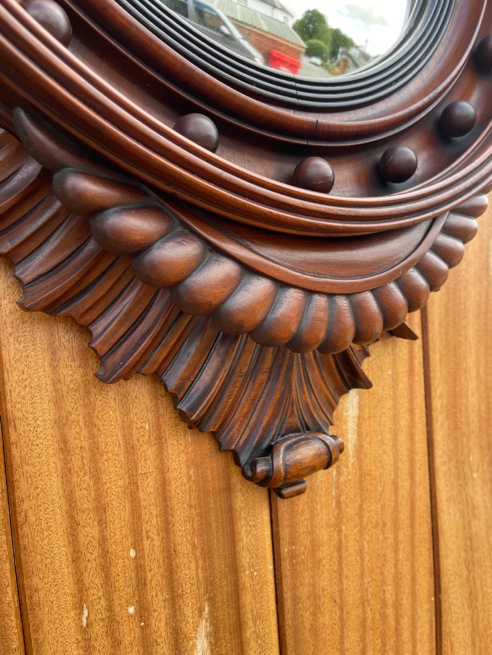A carved dark timber convex wall mirror featuring a crested eagle surmount, spherical frame embellishments, and a circular convex glass plate. View IV