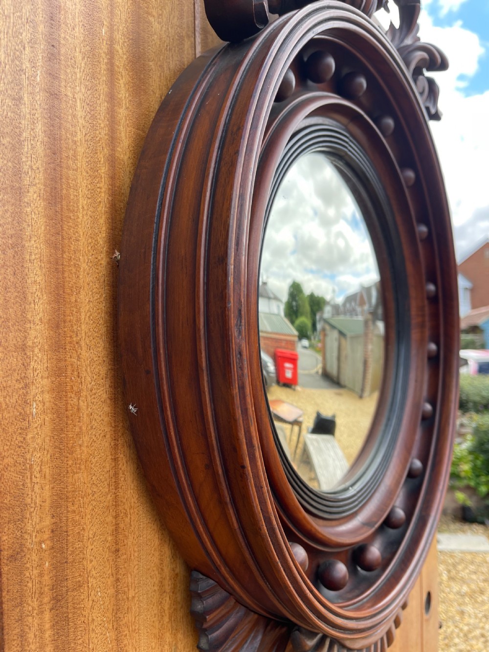 A carved dark timber convex wall mirror featuring a crested eagle surmount, spherical frame embellishments, and a circular convex glass plate. View V