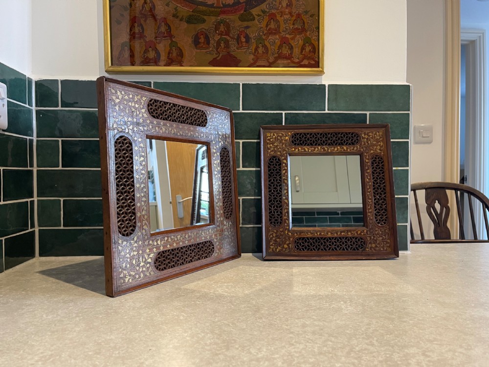 A pair of square dark wood framed mirrors featuring intricate floral brass inlay and pierced geometric jaali lattice panels.
