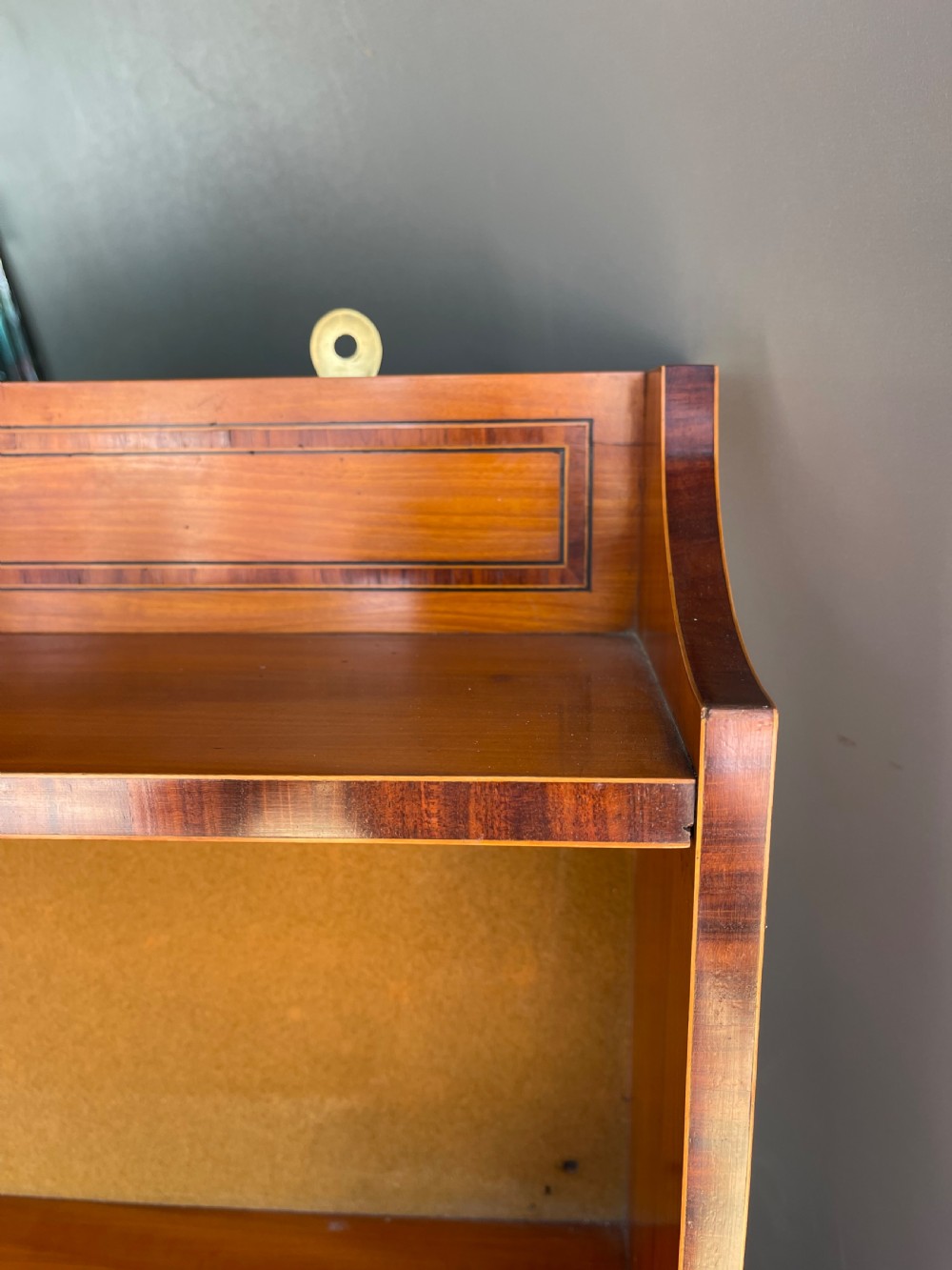 An antique satinwood hanging shelf unit featuring an arched cresting rail, three open tiers, and two drawers at the base with brass drop ring handles. View II