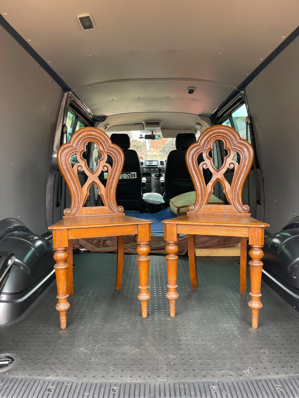 A pair of 19th-century oak hall chairs featuring carved pierced backrests, flat solid wooden seats, and turned front legs.