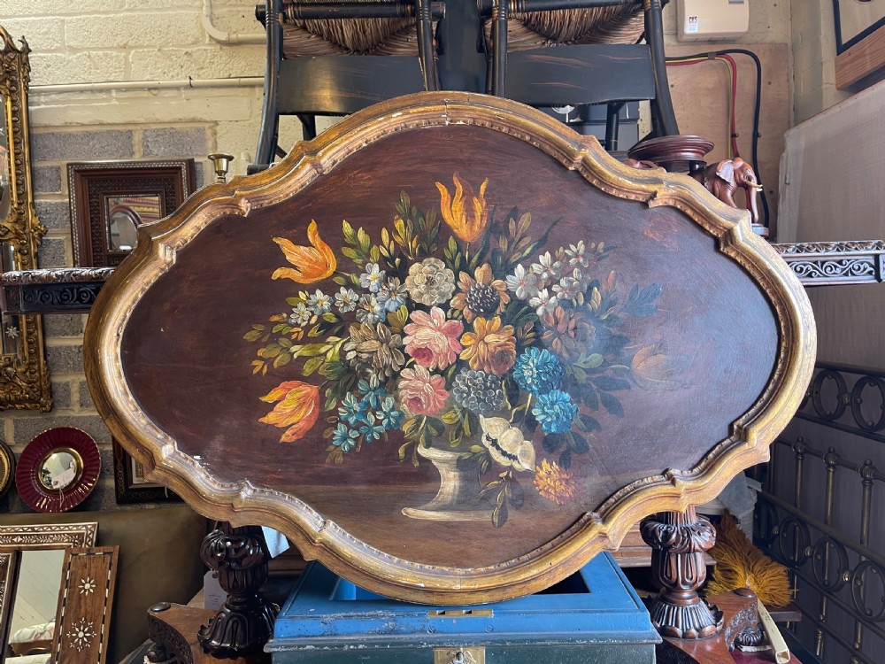 An oval-shaped Italian floral still life painting on a wooden board, depicting colourful flowers in a classical urn inside a moulded gold frame.