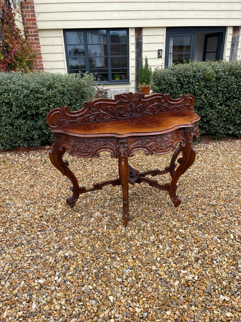 An ornate carved dark rosewood console table featuring an elaborate scrollwork backboard, shaped top, and intricately carved cabriole legs with stretchers.