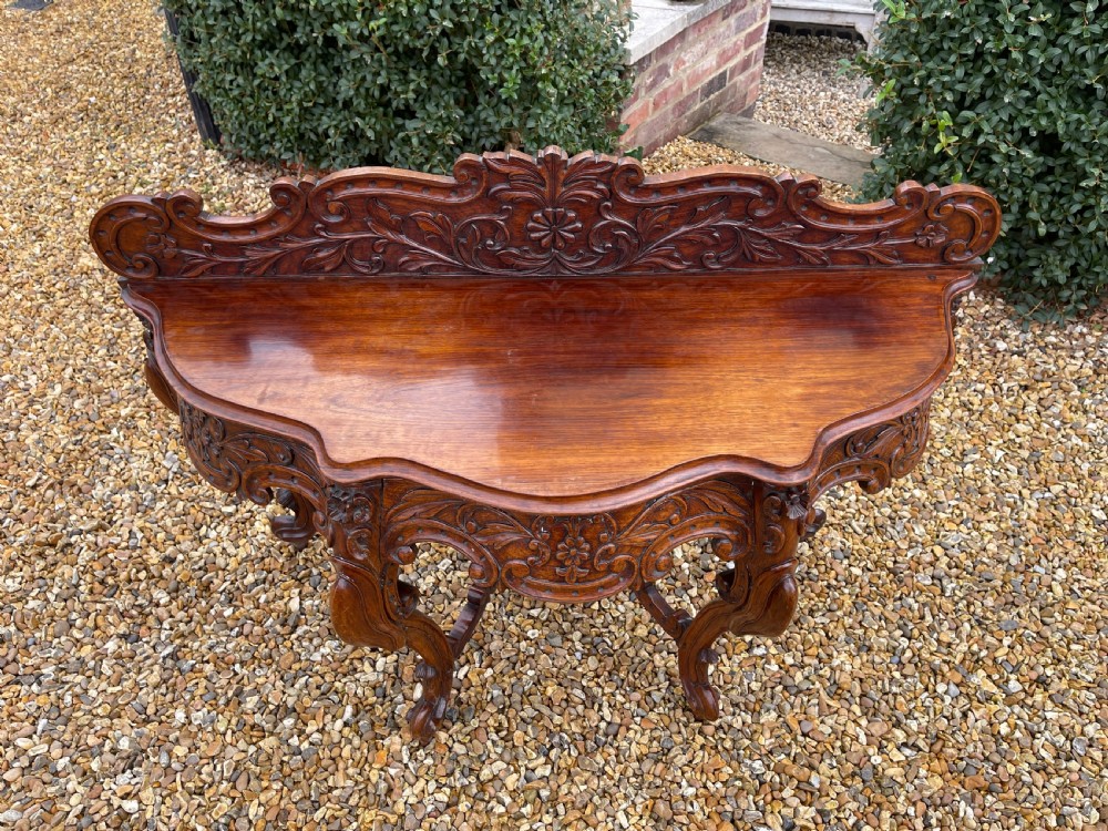 An ornate carved dark rosewood console table featuring an elaborate scrollwork backboard, shaped top, and intricately carved cabriole legs with stretchers. View V
