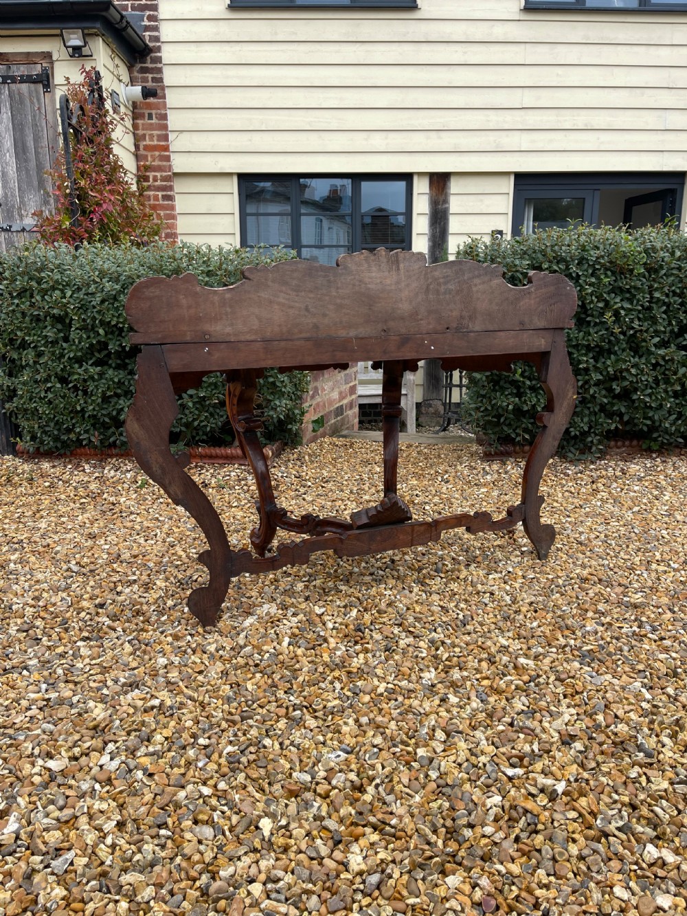 An ornate carved dark rosewood console table featuring an elaborate scrollwork backboard, shaped top, and intricately carved cabriole legs with stretchers. View VI