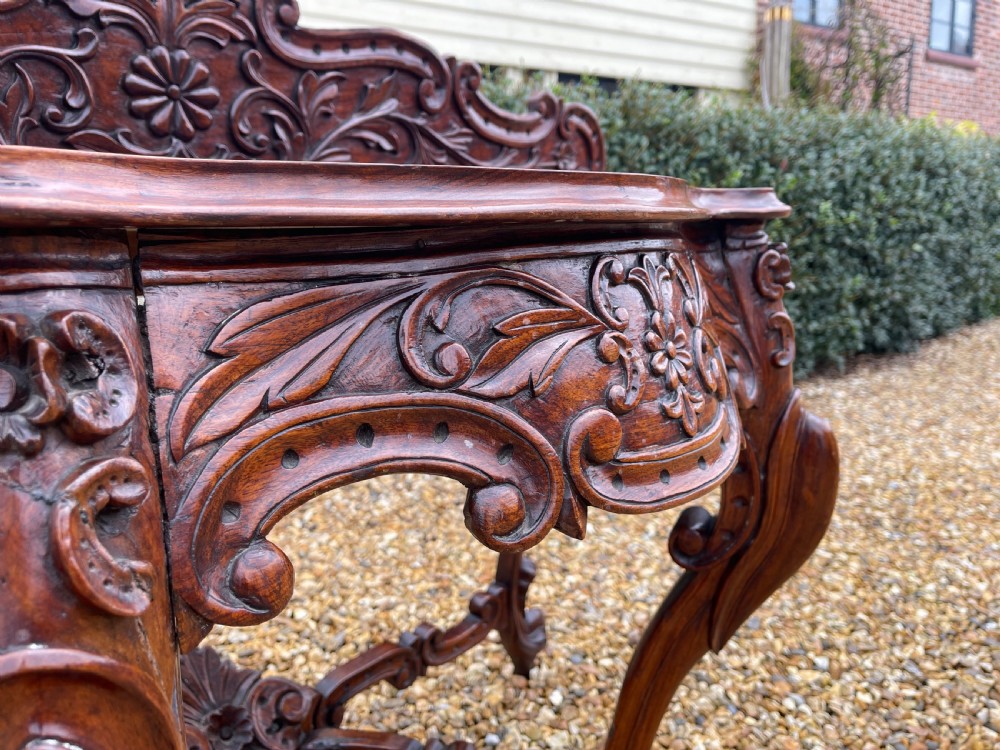 An ornate carved dark rosewood console table featuring an elaborate scrollwork backboard, shaped top, and intricately carved cabriole legs with stretchers. View VII